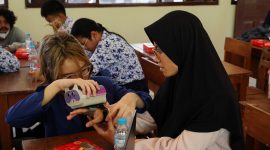 Salah satu anggota tim inovator ITS, Firania Putri Harsanti, mempraktikkan cara menggunakan Neutrack AI Glove pada salah satu siswa SMPLB-A YPAB Surabaya. Foto: ITS