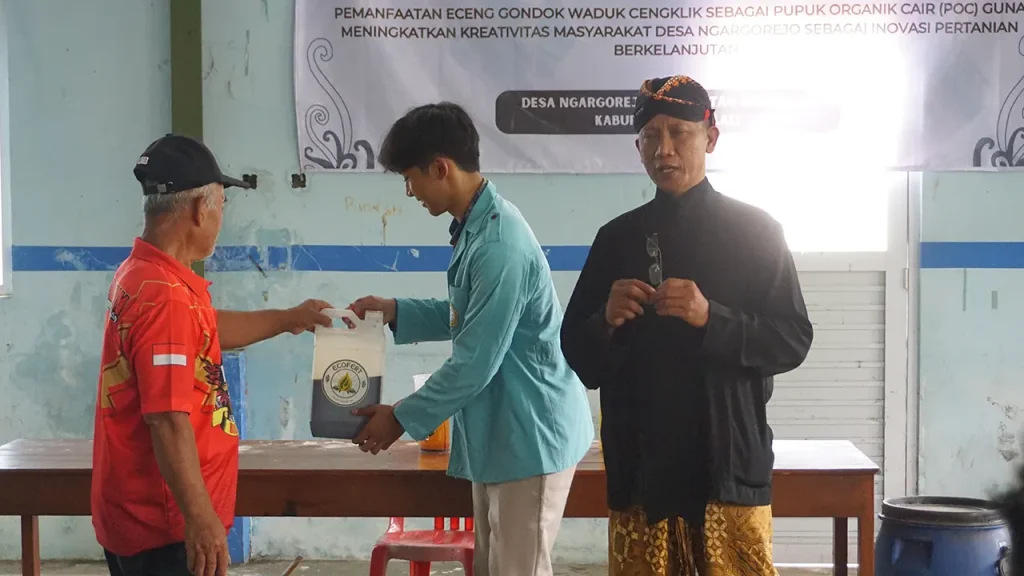 Seorang mahasiswa Universitas Sebelas Maret (UNS) menyerahkan contoh pupuk organik cair hasil olahan eceng gondok Waduk Cengklik kepada warga Desa Ngargorejo, Kecamatan Ngemplak, Kabupaten Boyolali, dalam kegiatan sosialisasi dan pelatihan pemanfaatan eceng gondok sebagai inovasi pertanian berkelanjutan, Rabu (11/12/2025). Foto: pribadi
