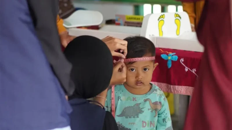 Seorang balita menjalani pengukuran lingkar kepala oleh petugas saat kegiatan posyandu di Desa Geneng, Ngawi. Pemeriksaan ini menjadi bagian dari upaya deteksi dini stunting dan pemantauan tumbuh kembang anak. Foto: Dokumentasi pribadi Kelompok 97 KKN UNS